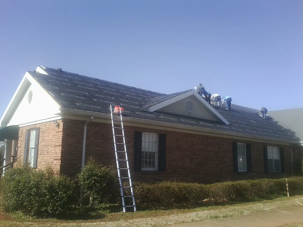 Crew tearing shingles off a brick ranch roof with a ladder set — Emergency Roof Repair work by our crew in Galt