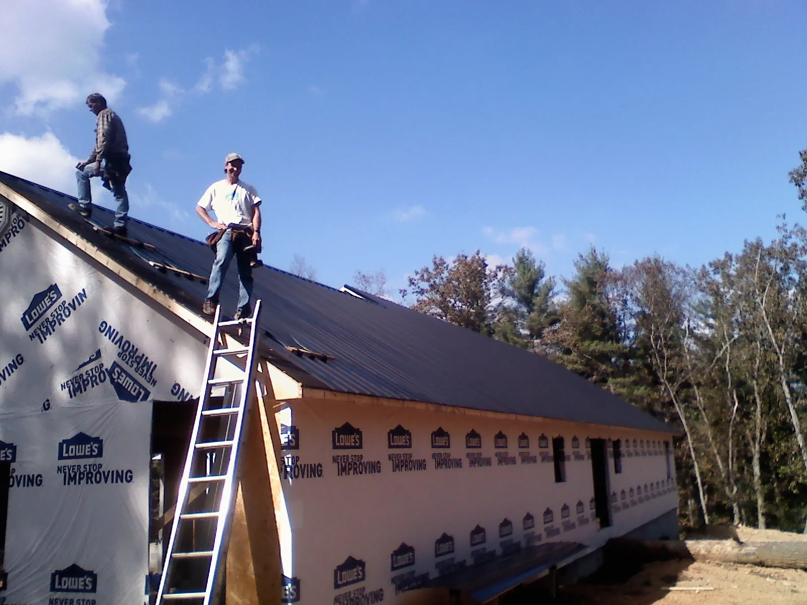Two roofers standing on a long dark metal roof over a wrapped building in Galt