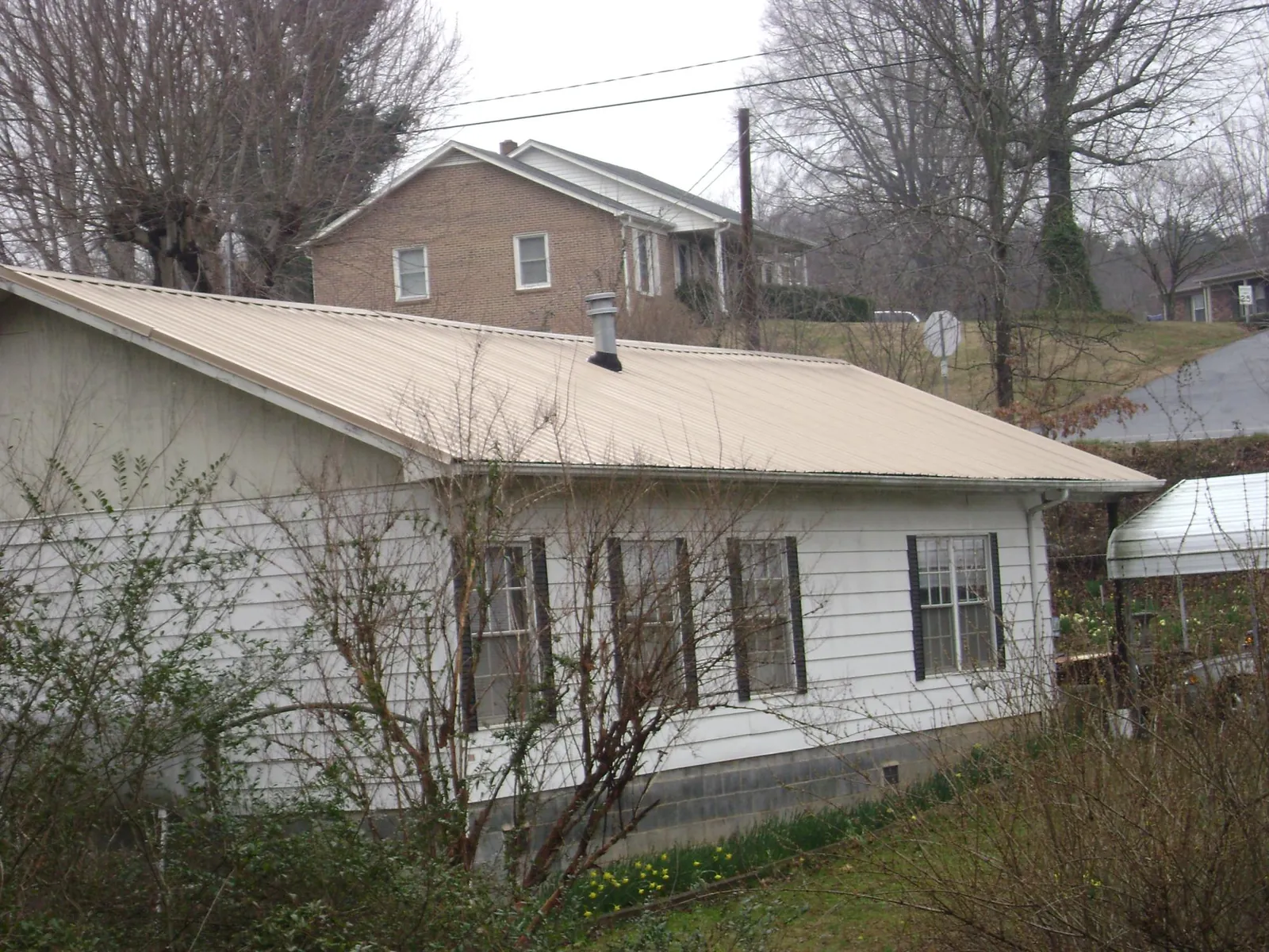 Tan metal roof on a white sided house set into a hillside — Commercial Roofing by Roofing Brothers in Galt